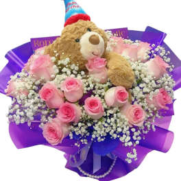 Pink roses arranged with a teddy bear in a birthday hat