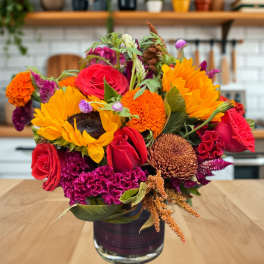 Mixed bouquet of sunflowers, red roses, and orange blooms in a glass vase