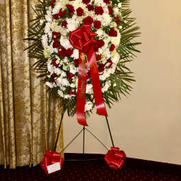 Standing floral wreath of red and white flowers with a red ribbon