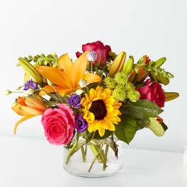 Colorful bouquet of roses, lilies, and a sunflower in a glass vase