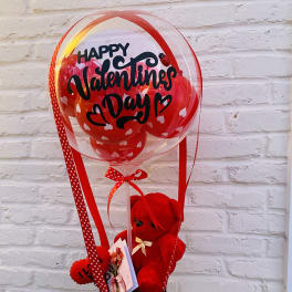 Valentine's Day balloon arrangement with a red teddy bear in a black basket