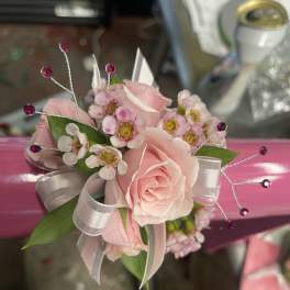 Pink rose corsage with small white blossoms and ribbon