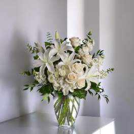 White lilies and cream roses arranged in a clear glass vase