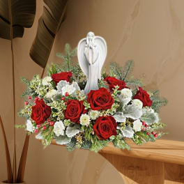 Red roses and white flowers arranged around a white angel figurine