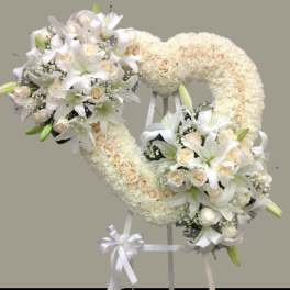 Heart-shaped white floral wreath on a stand with ribbon