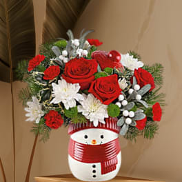Red and white floral arrangement in a snowman vase with a red scarf