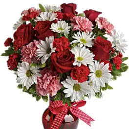 Red roses and white daisies in a red vase with a polka-dot ribbon