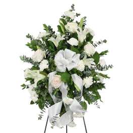 White floral standing spray with lilies, roses, and ribbon on an easel