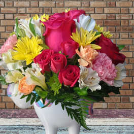 Bouquet of pink roses, yellow daisies, and white lilies in a white ceramic vase