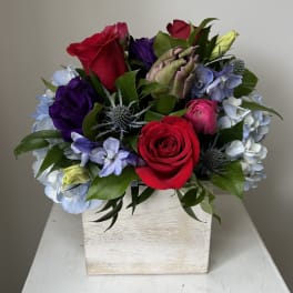 Mixed bouquet of roses, hydrangeas, and purple blooms in a white wooden box