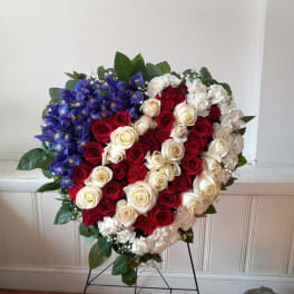 Heart-shaped floral tribute with red, white, and blue flowers on a stand