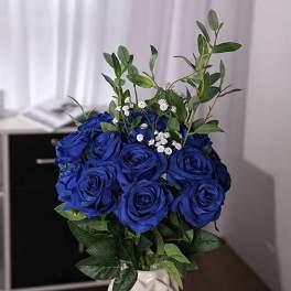 Blue rose bouquet in a white vase with green foliage