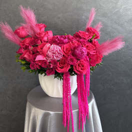 Hot pink rose arrangement in a white vase with pink feather accents