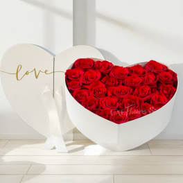 Heart-shaped box of red roses beside a white heart display with the word love