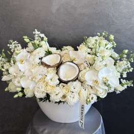 White floral arrangement with orchids, roses, and coconut halves in a white bowl