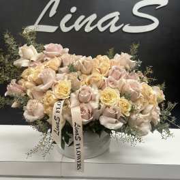 Large pastel rose arrangement in a white bowl vase with ribbon tags