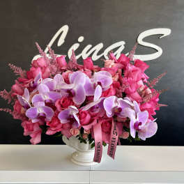 Pink roses and lavender orchids in a white pedestal vase