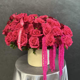 Pink and burgundy roses arranged in a cream hat box with hanging pink amaranthus