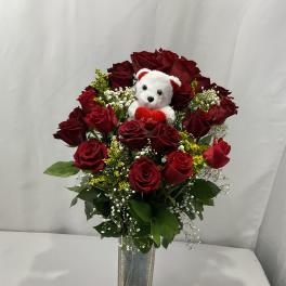 Red rose bouquet in a clear vase with a small teddy bear
