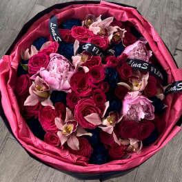 Round bouquet of pink, blue, and pale flowers wrapped in bright pink paper