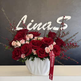 Red and blush roses arranged in a white vase with a red ribbon