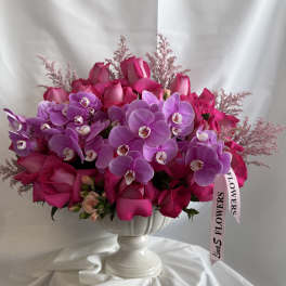Pink roses and purple orchids arranged in a white pedestal vase