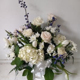 White and pale pink floral arrangement with blue accents in a white vase