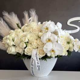 Cream roses and white orchids arranged in a textured white vase.