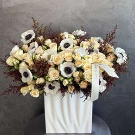 Cream roses and white anemones arranged in a white vase