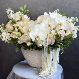 White orchids and pale roses in a textured vase with trailing white strands