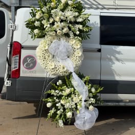 White floral funeral wreath and spray with ribbon on a stand