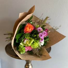 Wrapped bouquet of mixed flowers with an orange rose and pink blooms