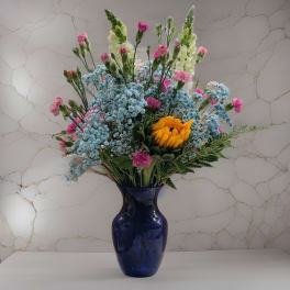 Mixed bouquet with blue, pink, and yellow flowers in a dark blue vase