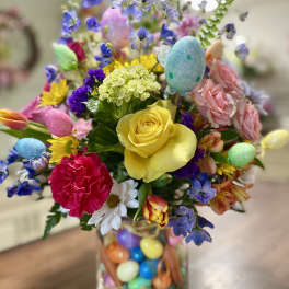 Colorful bouquet with roses, carnations, daisies, and pastel Easter eggs in a glass vase