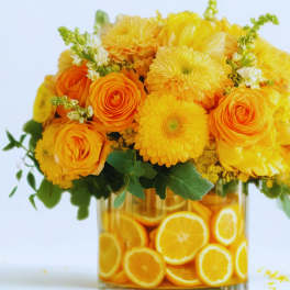 Yellow and orange flower arrangement in a glass vase filled with orange slices