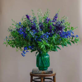Blue and purple flower arrangement in a green glass vase