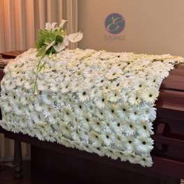 White flower-covered casket with a small white floral spray