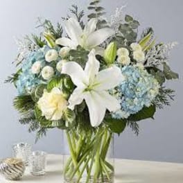 White lilies and blue hydrangeas in a clear glass vase