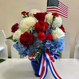 Red and white roses with blue hydrangeas in a vase, topped with an American flag