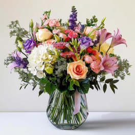 Mixed bouquet of roses, lilies, and orchids in a glass vase