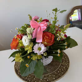 Mixed bouquet of roses, daisies, and alstroemeria in a white basket with a pink bow