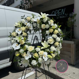 White floral wreath on a black stand with roses and lilies