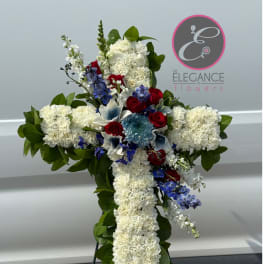 Cross-shaped floral tribute with white carnations, red roses, and blue accents