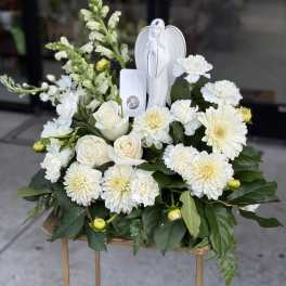 White floral sympathy arrangement with roses, chrysanthemums, and an angel figurine