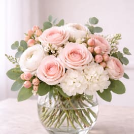 Blush roses and white blooms arranged in a clear glass vase