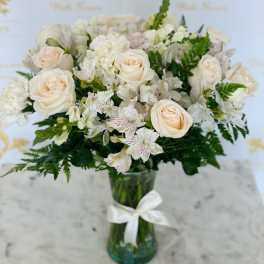 Cream roses and white flowers in a glass vase with a white ribbon