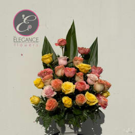 Mixed roses in a white pedestal vase with tall green leaves