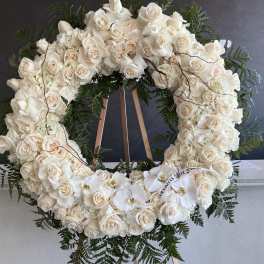 Large white rose wreath on a wooden easel with orchids and greenery