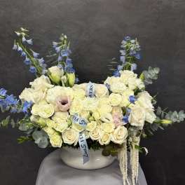 White rose arrangement with blue delphinium in a white vase