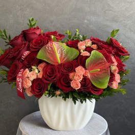 Red roses and peach spray roses in a white vase with anthuriums